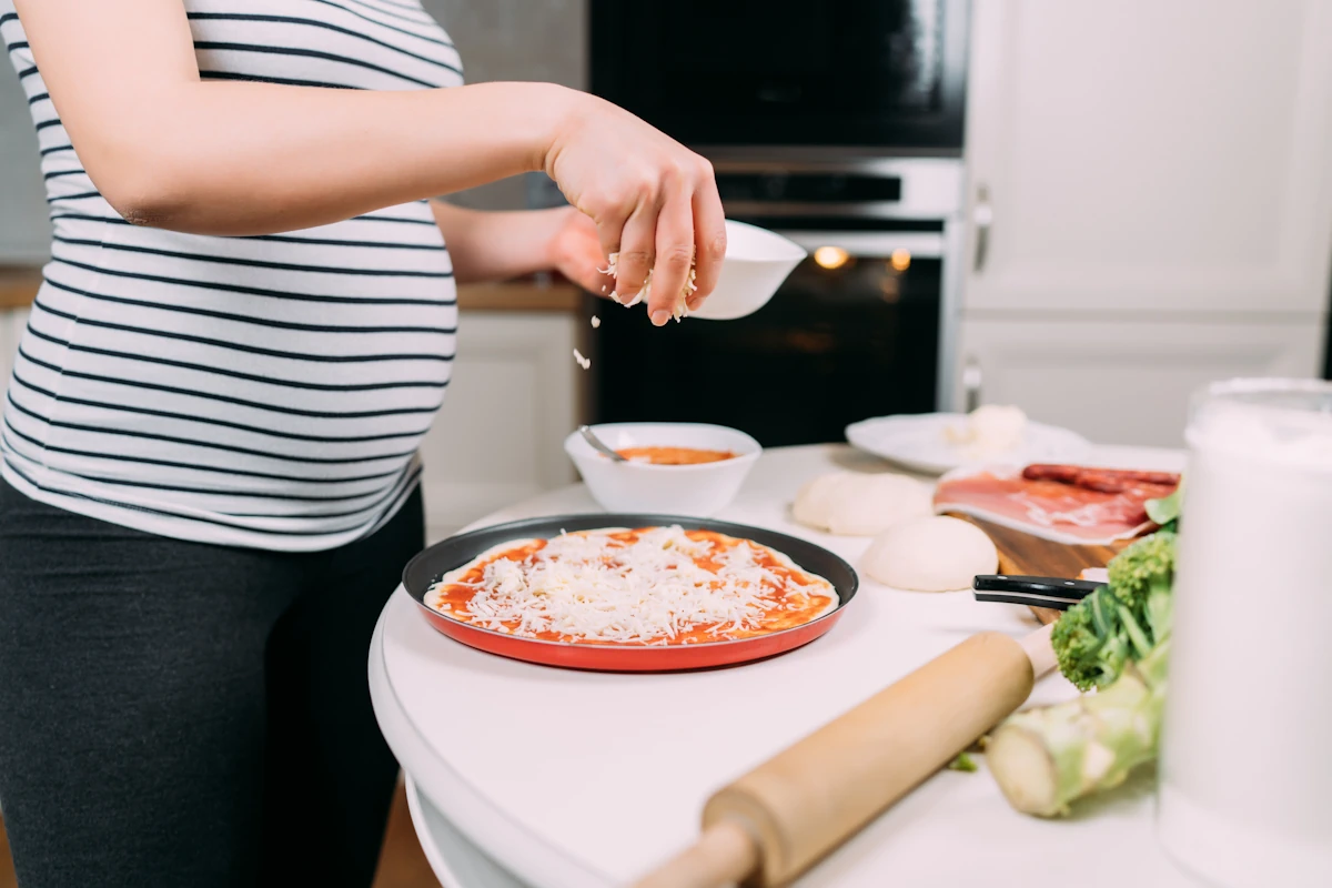 Une femme enceinte qui prépare une pizza dans sa cuisine