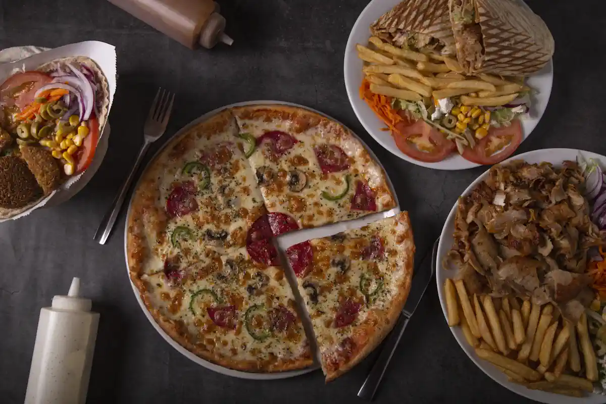 Une table bien garnie avec une pizza une assiette de frittes et de kebab