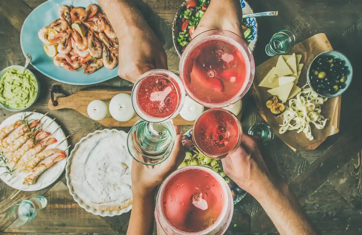 Des amis autour d'une table bien garnis qui lèvent leur verre rempli de différents boissons