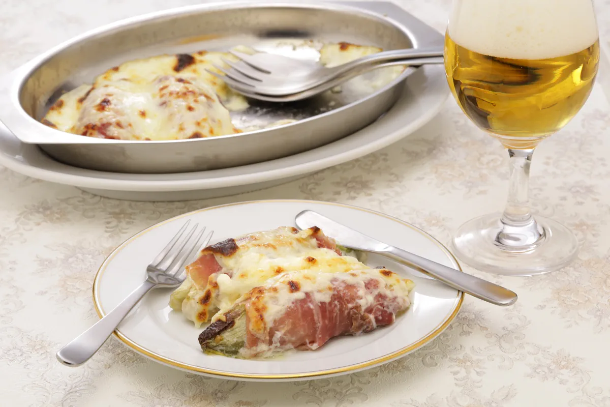 Une assiette d'endives aux jambons posé à coté d'un verre de vin et d'un plat de gratin