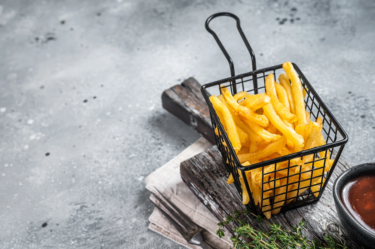 Des frites dans un petit bac noir posé sur une plaque en bois