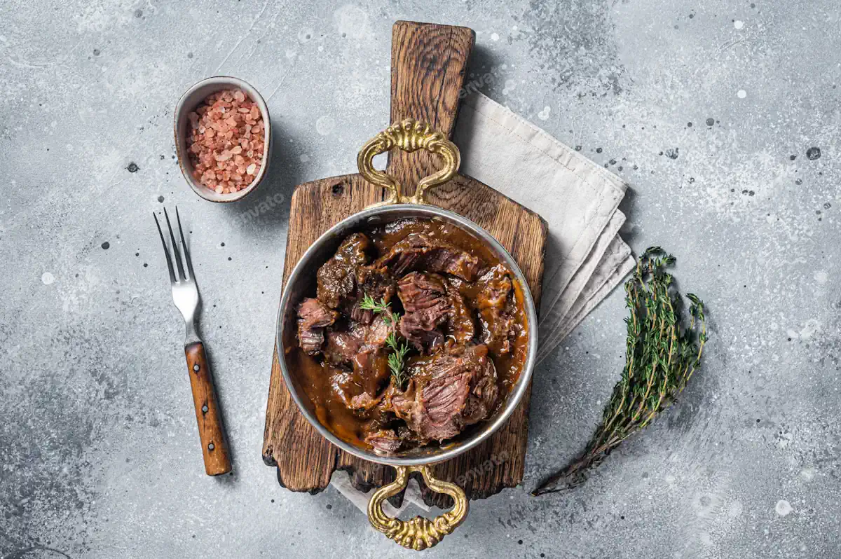 Plat de viande avec sauce fond de veau posé sur une plaque en bois à côté d'une fourchette