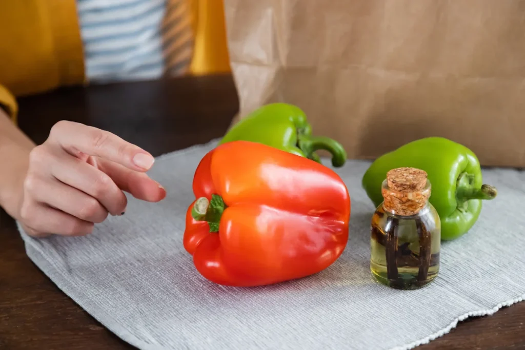Une personne face à un poivron rouge et des poivrons verts et une bouteille d'huile