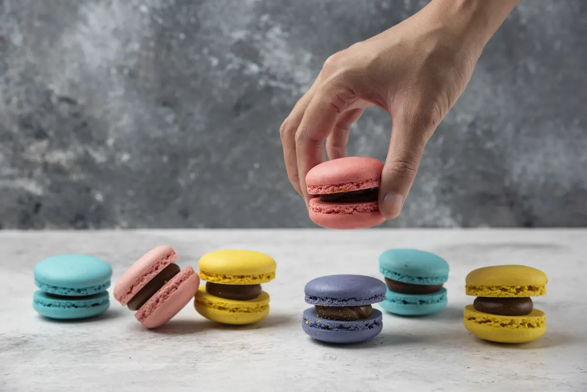Une personne qui prend un macaron sur une pile de plusieurs macarons colorés