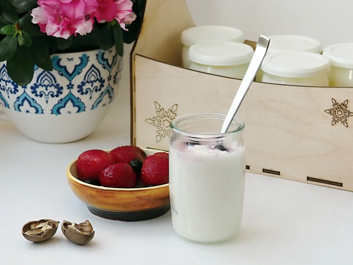 Un pot de yaourt posé à côté d'une assiette de fruits et d'un bac avec d'autres yaourts