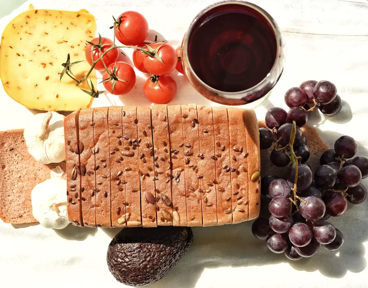 Un morceau de fromage à côté d'un verre de vin, de tomates et d'un pin avec du raisin