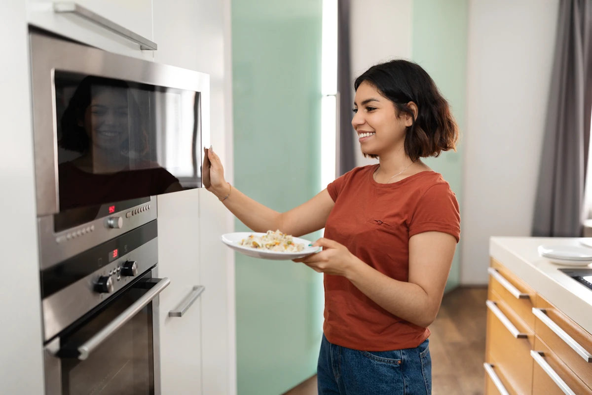 Une femme qui ouvre la partie mirco-onde de son four pour y mettre une assiette