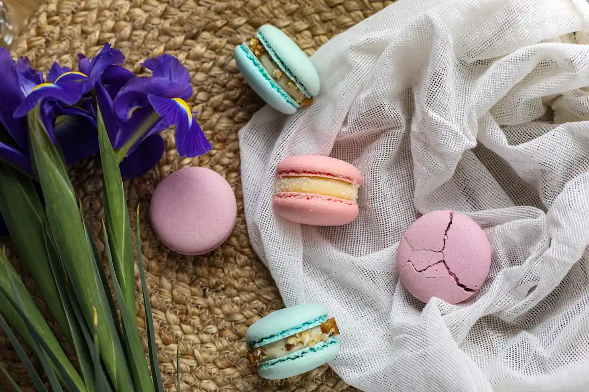 Des macarons posés sur une surface en liège et un voile à côté d'un bouquet de fleur bleues