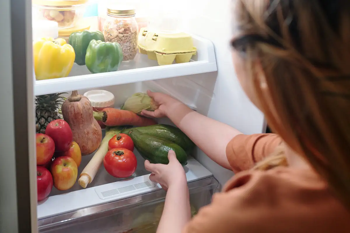 Une femme qui met des légumes dans son réfrigérateur