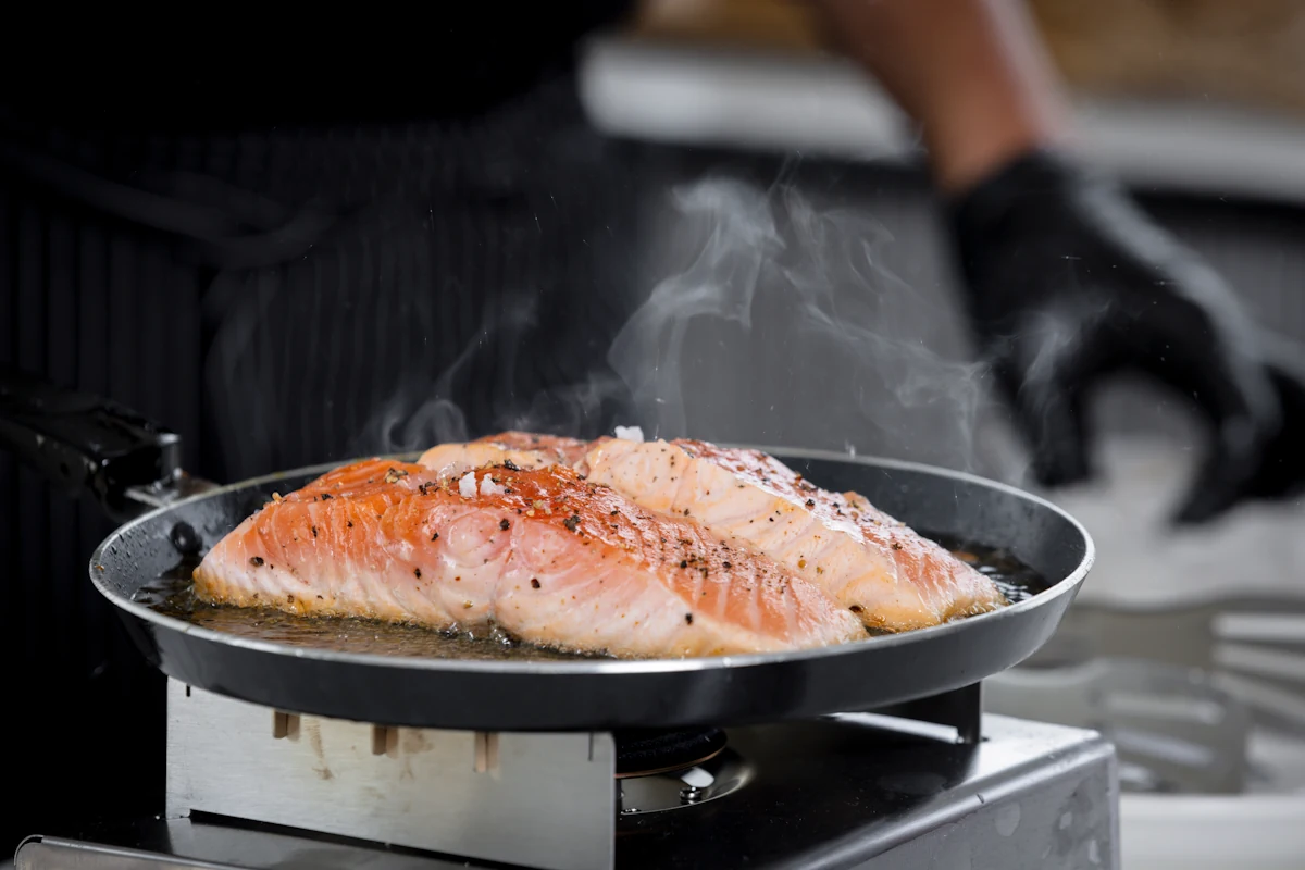 Une personne qui cuit des poissons à la poêle