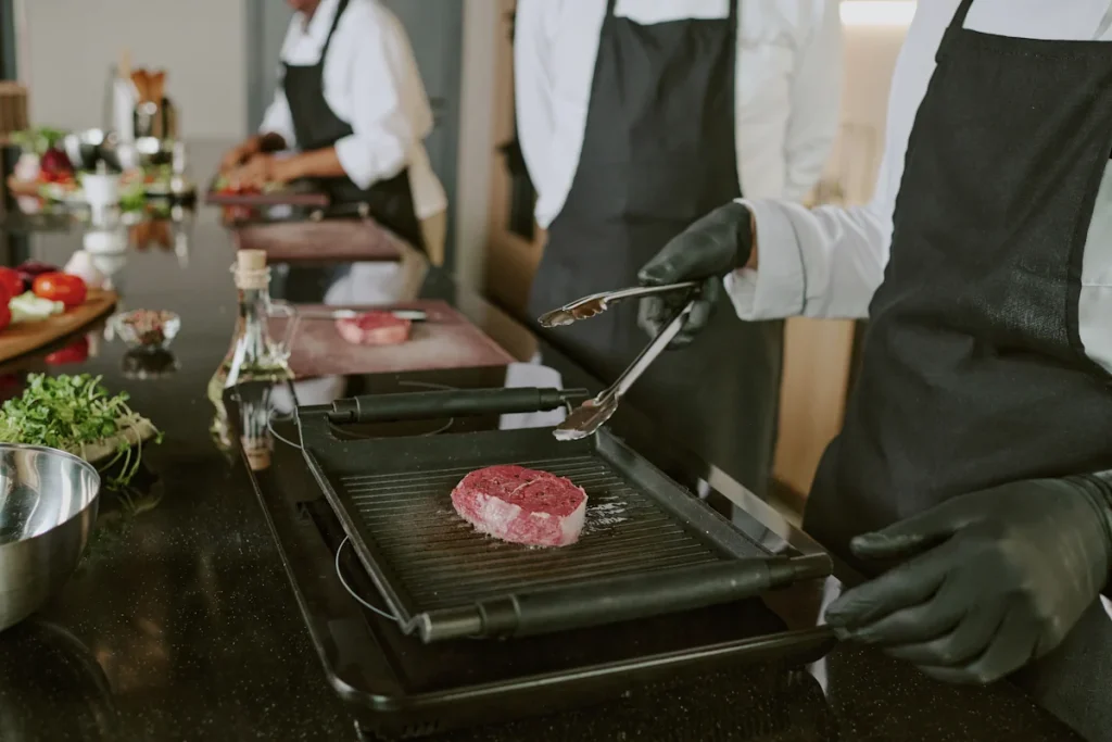 Des personnes en tablier noir qui cuit un morceau de viande sur un barbecue