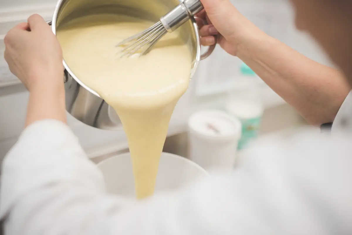 Une personne qui verse de la crème pâtissière dans un contenant