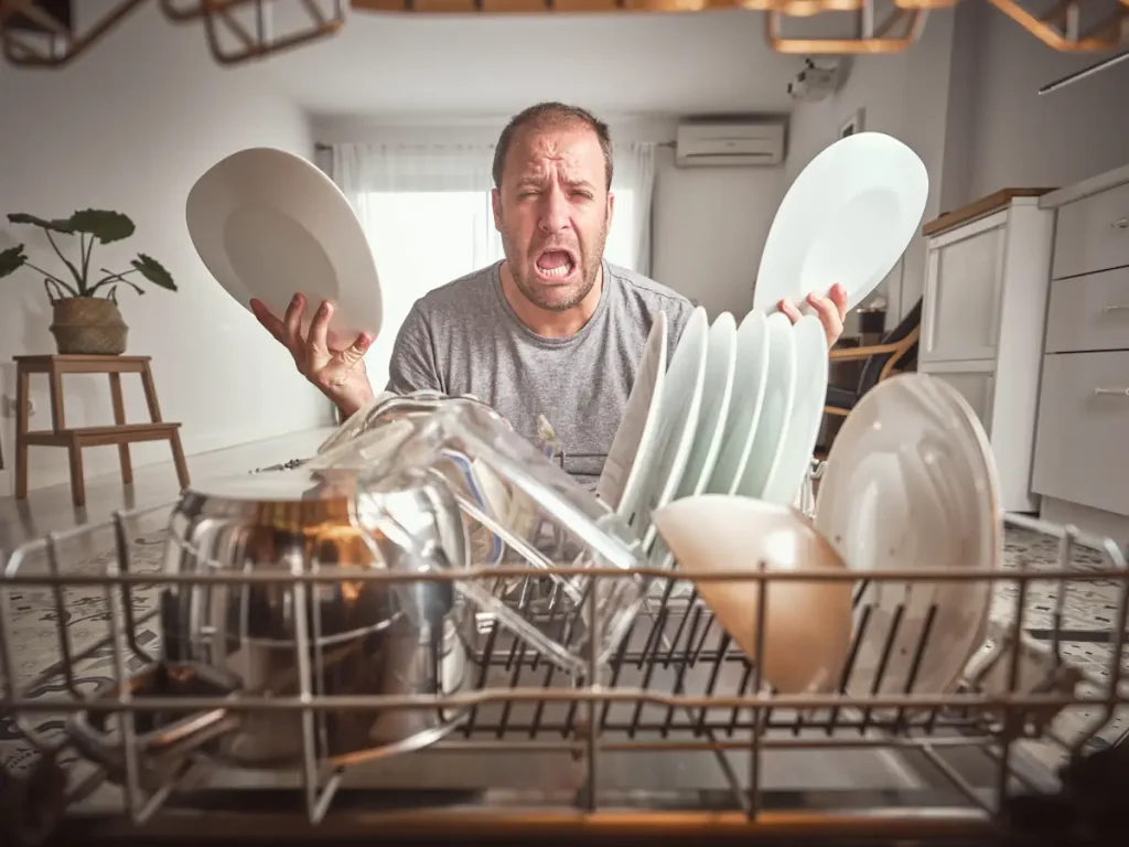 Un homme qui fait la grimace en sortant des assiettes du lave-vaisselle