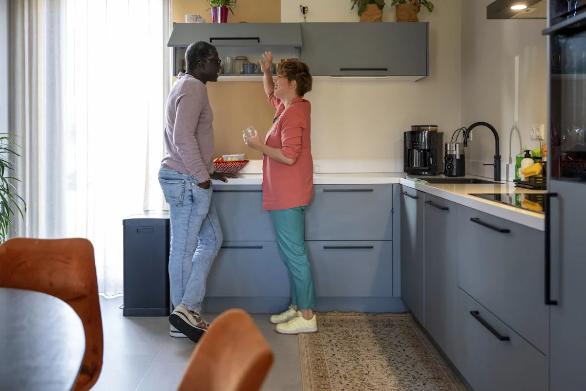 Une femme et un homme qui dicutent en ouvrant un meuble en hauteur dans une petite cuisine