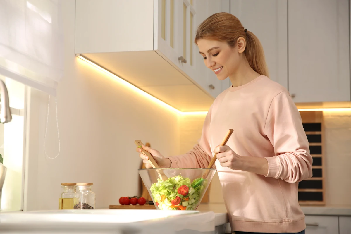 Une femme qui prépare une salade sur un plan de travail éclairé avec de rubans LED