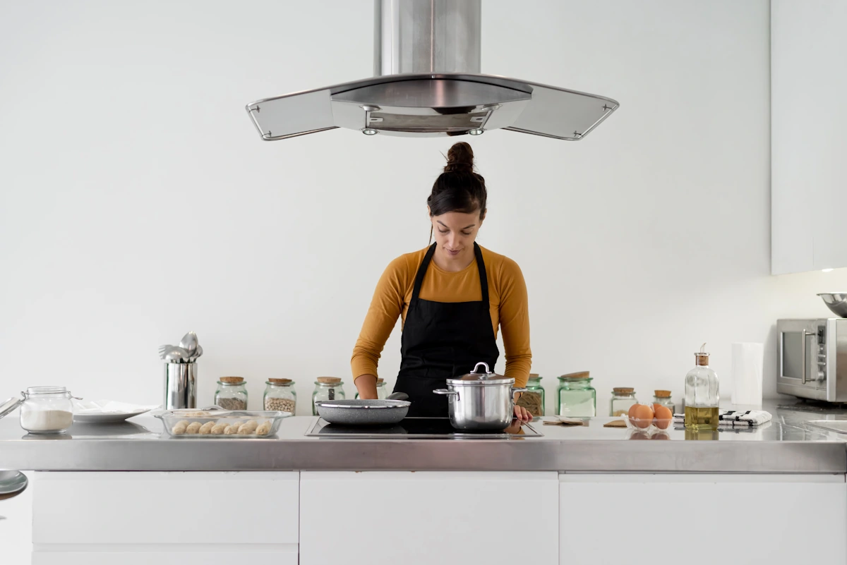 Une femme qui cuisine avec une hotte aspirante au dessus d'elle