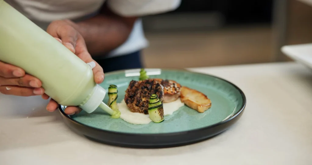 Une personne qui dresse une assiette en cuisine avec sauce