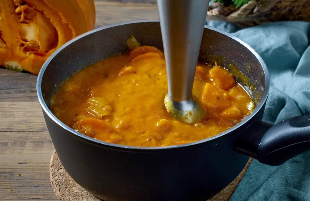 Une personne qui utilise un mixeur plongeant pour faire une soupe