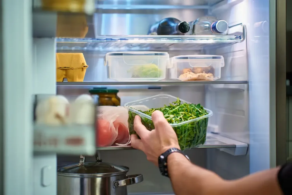Une personne qui range des légumes cuits dans le réfrigérateur