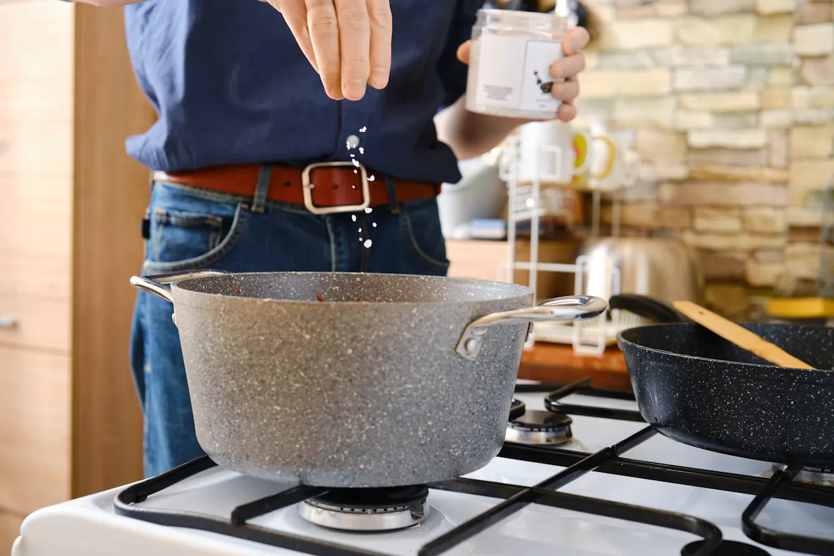 Une personne qui ajoute du bicarbonate de soude dans une sauce pour corriger l'acidité
