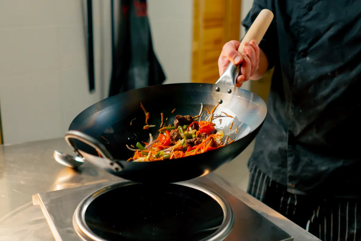 Une personne qui cuisine avec un wok sur une plaque à induction